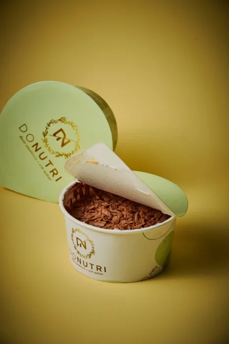 Pote DONUTRI aberto com mousse de chocolate e raspas, tampa verde com o monograma dourado